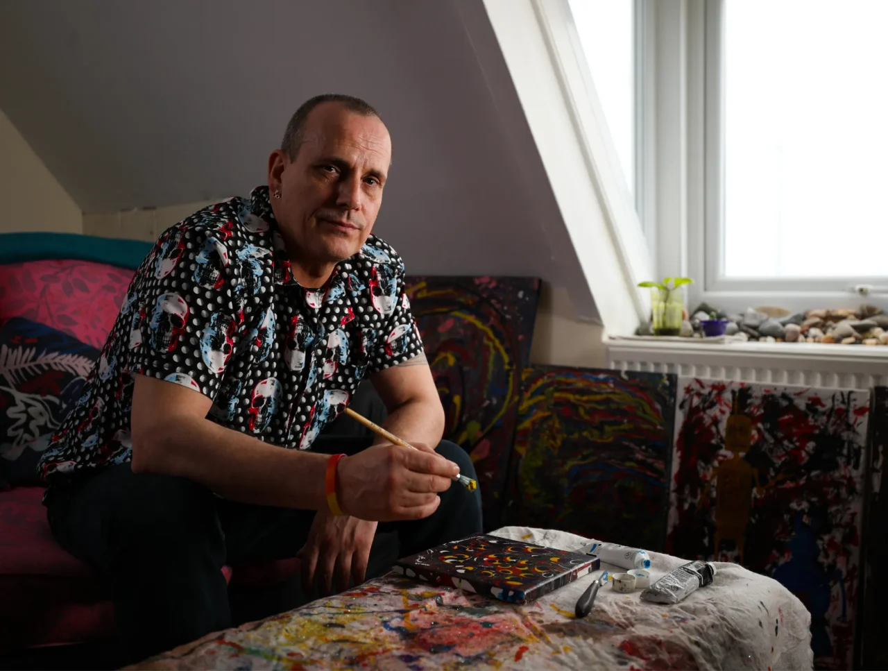Portrait photo of a male UK Armed Forces veteran holding a paintbrush above a canvas.