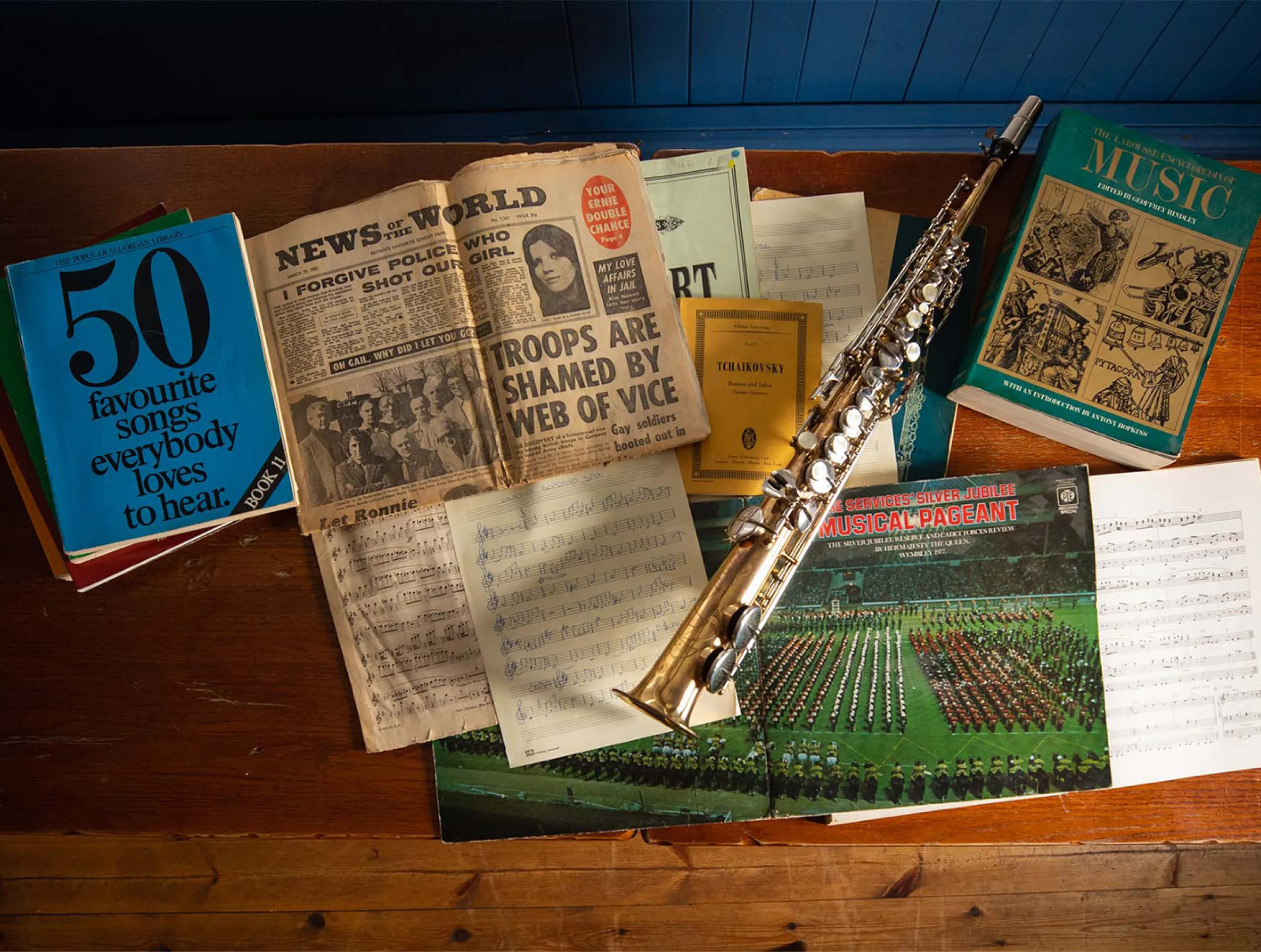 Photo of a straight soprano saxophone, various musical notation sheets, two music books and an old newspaper front page.